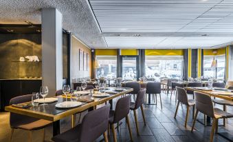 a modern restaurant with yellow and gray color scheme , black chairs , and white tablecloths on tables at Hotel le Morgane