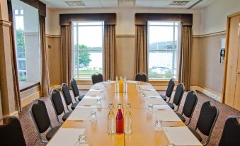 a long wooden table with white plates , glasses , and water bottles is set up in a conference room at Low Wood Bay