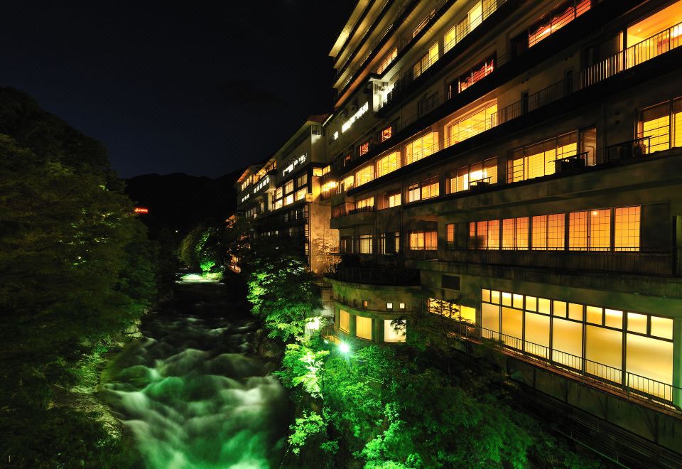 a nighttime view of a river flowing through a city , illuminated by green lights and surrounded by buildings at Zazan Minakami