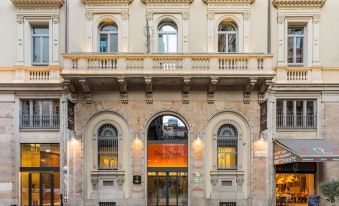 a grand , ornate building with an arched entrance and red signage , situated in the heart of a bustling city at Room Mate Giulia