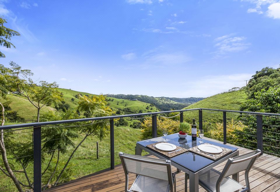 a wooden deck overlooking a lush green hillside , with a dining table and chairs set up for a meal at Top of the Hill