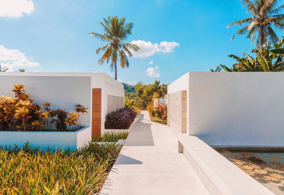 a white house with a walkway leading up to it , surrounded by palm trees and a blue sky at Origin Lombok