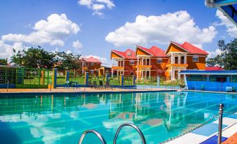 a large outdoor swimming pool surrounded by several orange houses , with blue skies and clouds in the background at Country Inn Masindi