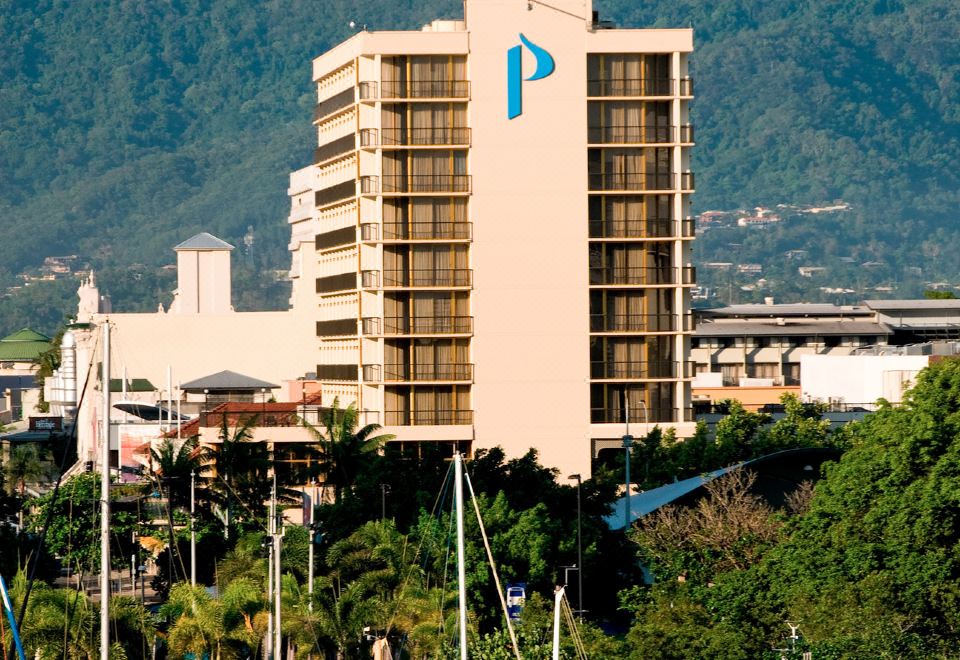 "a tall building with a blue "" p "" on top is surrounded by trees and mountains" at Pacific Hotel Cairns