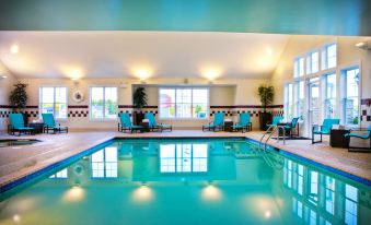an indoor swimming pool with a large window , surrounded by chairs and tables , in a well - lit room at Residence Inn Auburn