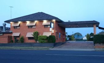 a brick building with an awning and a covered walkway , situated on the side of a road at Adelong Motel