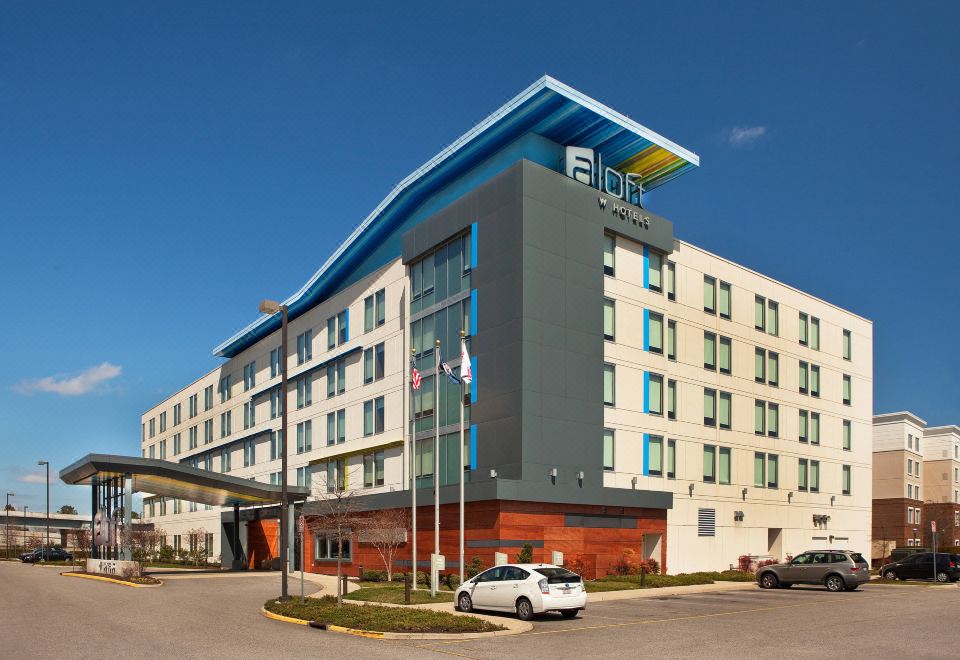 a modern hotel with a blue roof and white columns , surrounded by cars and trees at Aloft Chesapeake
