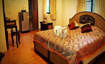 a large bed with a floral bedspread and two white teddy bears on it , set in a hotel room at Phufatara Resort