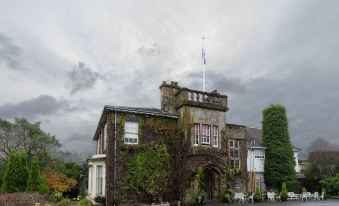 a large stone building with an ivy - covered entrance and a flag pole , set against a cloudy sky at Dalmeny Park House Hotel
