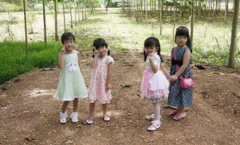 a group of four young girls in dresses are standing together on a dirt path , posing for a picture at Tonnam Resort