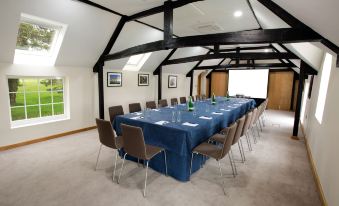 a long dining table with blue tablecloth and chairs set up for a meeting in a room with wooden beams and windows at Sandford Springs Hotel and Golf Club