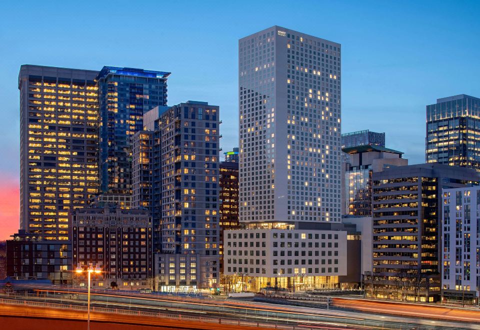a city skyline at dusk , with tall buildings lit up and a highway visible in the foreground at Hyatt Regency Seattle