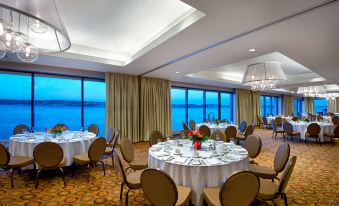 a well - decorated banquet hall with round tables and chairs arranged for a formal event , overlooking the ocean at Halifax Marriott Harbourfront Hotel