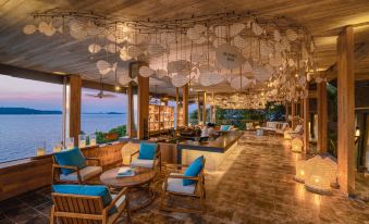 a modern restaurant with wooden ceiling , blue couches , and a view of the ocean , decorated with hanging lights at Six Senses Krabey Island