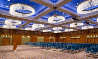 a large conference room with blue chairs arranged in rows and chandeliers hanging from the ceiling at Radisson Blu M'Bamou Palace Hotel, Brazzaville