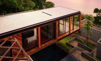a modern house with a large glass window overlooking a pool , surrounded by lush greenery at The Naka Phuket