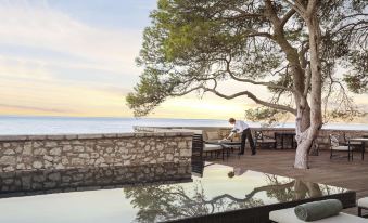a man sitting on a patio overlooking the ocean , with a tree and a table in the foreground at Aman Sveti Stefan