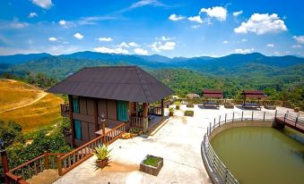 a beautiful mountainous landscape with a wooden house , a pond , and a tree , under a blue sky with clouds at The Waterway Villa