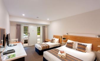 a hotel room with two beds , a desk , and a balcony door , all decorated in neutral colors at Berrima Bakehouse Motel