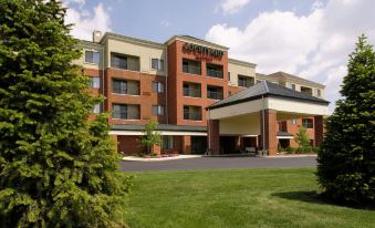 a courtyard by marriott hotel with a large sign above the entrance , surrounded by lush green grass and trees at Courtyard Akron Stow