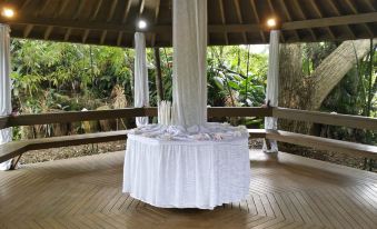 a white tablecloth on a round table covered in towels , surrounded by wooden chairs and surrounded by lush greenery at Rainforest Eco Lodge