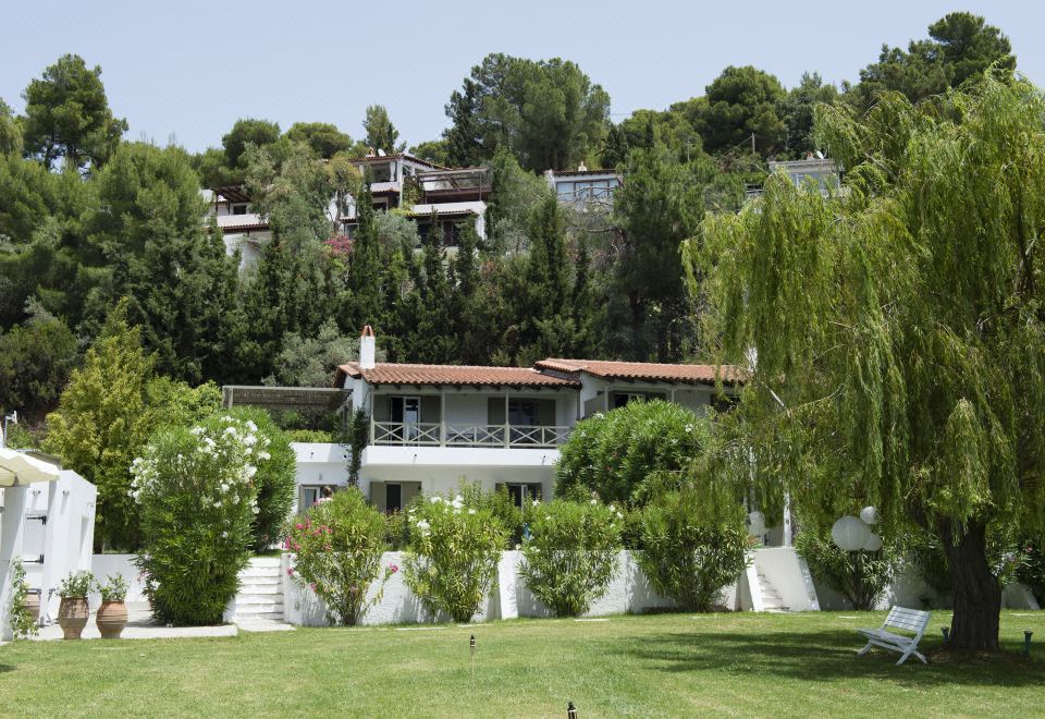 a large white house situated on a hillside , with trees and greenery surrounding the property at Skiathos Holidays Suites & Villas