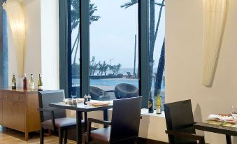 a restaurant with wooden tables and chairs , a large window , and a view of the ocean at Novotel Mumbai Juhu Beach