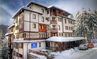 a large , two - story building with multiple balconies and windows , surrounded by snow - covered trees and mountains at Green Life Family Apartments Pamporovo