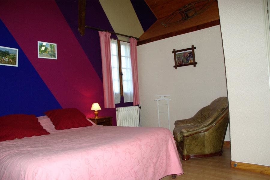 a bedroom with a bed , chair , and window has a pink and purple striped wall at L'Horizon