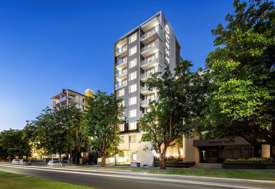 a tall building is surrounded by trees and street lamps , with a road in front of it at Quest Kings Park