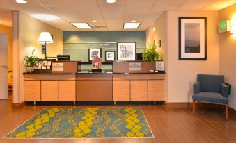 a reception area with a desk , chairs , and a rug , as well as framed pictures on the wall at Hampton Inn Portland East