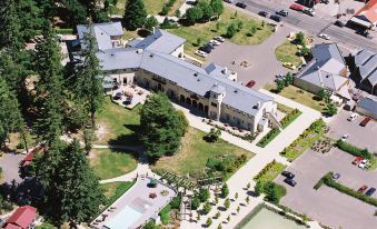 aerial view of a large building surrounded by trees and grass , with a pool in the foreground at Hanmer Springs Hotel