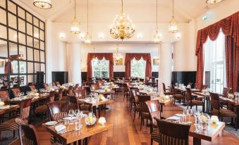 a large , elegant dining room with wooden floors , multiple tables set for a formal event , and chandeliers hanging from the ceiling at Low Wood Bay