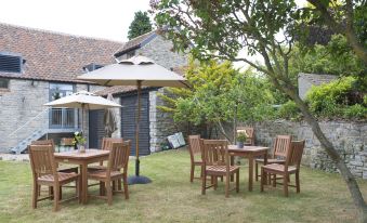 an outdoor dining area with a table , chairs , and umbrellas set up in a grassy area near a stone house at The White Hart