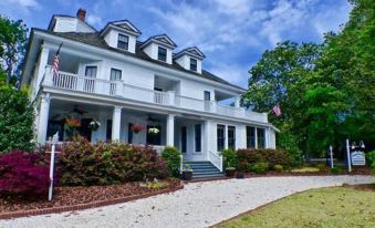 a large white house surrounded by a lush green lawn , with a gravel driveway leading up to the front door at Magnolia Inn