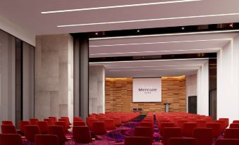 a large conference room with rows of red chairs arranged in front of a projector screen at Mercure Hai Phong