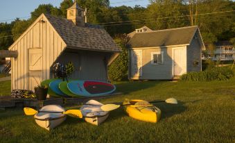 a group of kayaks and canoes are set up in a grassy area next to a small house at Lake Bomoseen Lodge