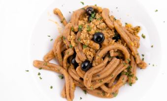 a plate of spaghetti topped with black olives and herbs , sitting on a white plate at Smy Civico Zero