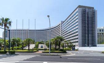 a large , modern building with a curved facade and multiple balconies , situated near a tree - lined street and surrounded by trees at Sheraton Grande Tokyo Bay Hotel