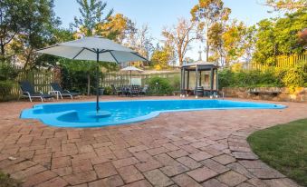 a backyard with a large , curved pool surrounded by patio furniture and umbrellas , creating a relaxing atmosphere at Holberry House