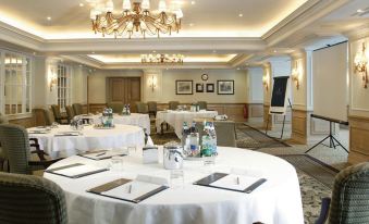 a large conference room with round tables and chairs , white tablecloths , and a chandelier hanging from the ceiling at Macdonald Compleat Angler