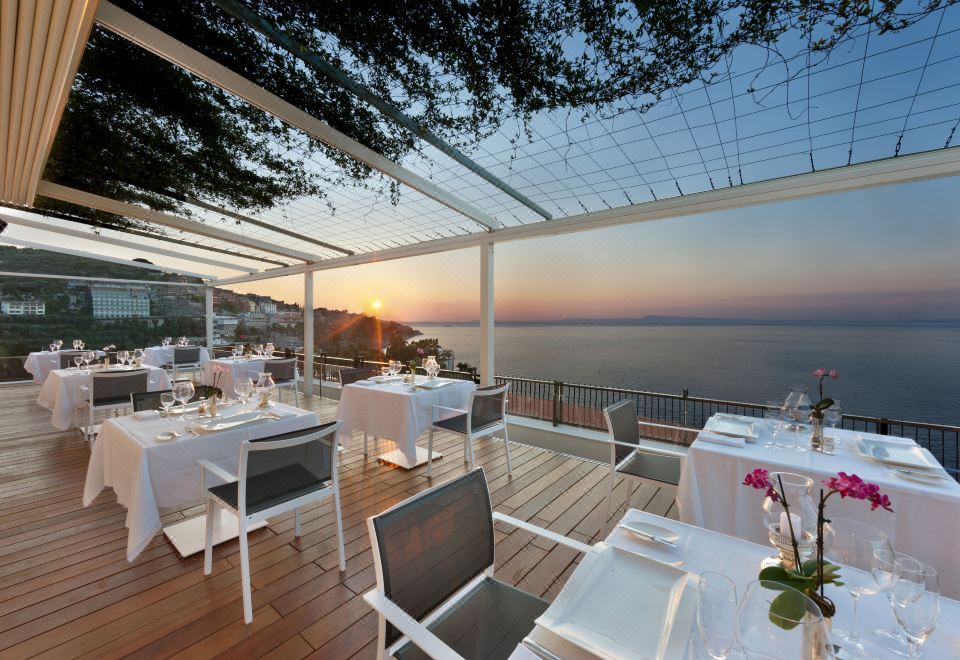 a rooftop dining area with tables and chairs , overlooking a body of water at sunset at Hotel Continental
