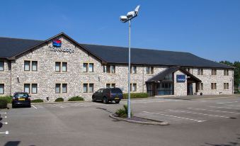 a brick building with a parking lot in front of it , and a car parked nearby at Travelodge Kendal