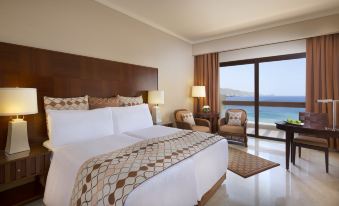 a hotel room with a large bed , two chairs , and a window overlooking the ocean at InterContinental Hotels Aqaba (Resort Aqaba)