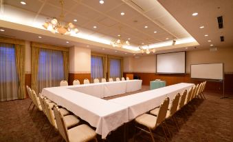 a large conference room with a long table surrounded by chairs and a projector screen at Hotel JAL City Aomori
