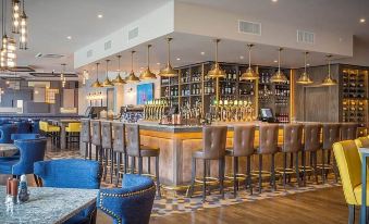 a modern bar with wooden flooring , blue chairs , and a long counter filled with bottles at Harbour Hotel