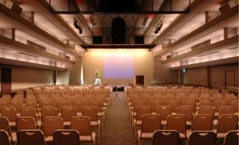 a large conference room with rows of chairs arranged in front of a projector screen at HOTEL MYSTAYS Utsunomiya
