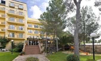 a yellow apartment building surrounded by trees , with stairs leading up to the entrance of the building at Bluesea Costa Verde