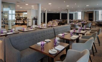 a restaurant with multiple dining tables and chairs , some of which are set up for customers at DoubleTree by Hilton London Heathrow Airport