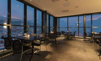 a restaurant with large windows offering a view of the city at night , and several tables and chairs arranged for dining at Scandic Narvik